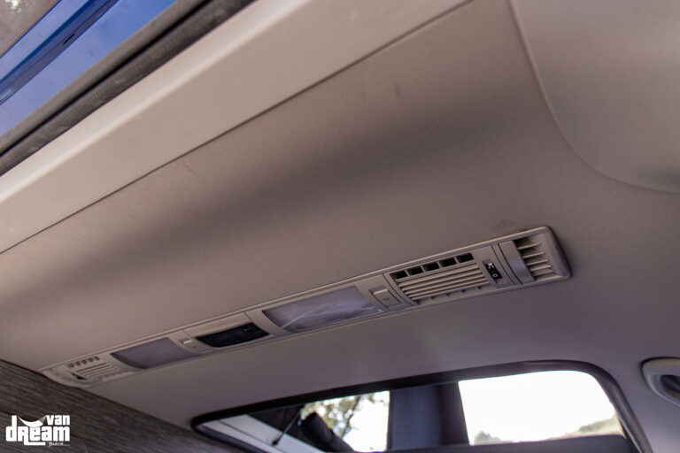 Detalle interior de la reubicación del climatizador original en la zona trasera de una Volkswagen T6.1 Caravelle con techo elevable BRAM.