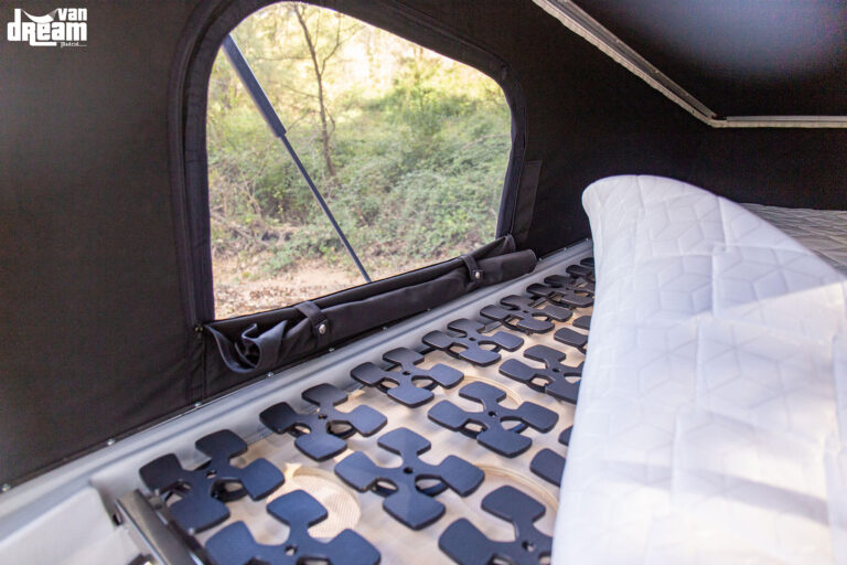 Detalle de la cama superior del techo elevable BRAM en una Volkswagen T6.1 Caravelle, con somier de muelles tipo Froli, colchón y ventana con mosquitera integrada.