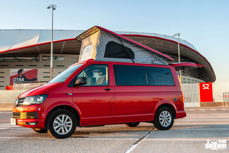 Vista lateral de una Volkswagen T6 Multivan roja con techo elevable Reimo abierto, lona gris y ventana lateral.