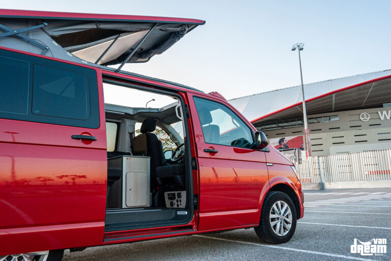 Vista lateral de una Volkswagen T6 Multivan roja con techo elevable Reimo abierto y lona panorámica Open Sky desplegada.
