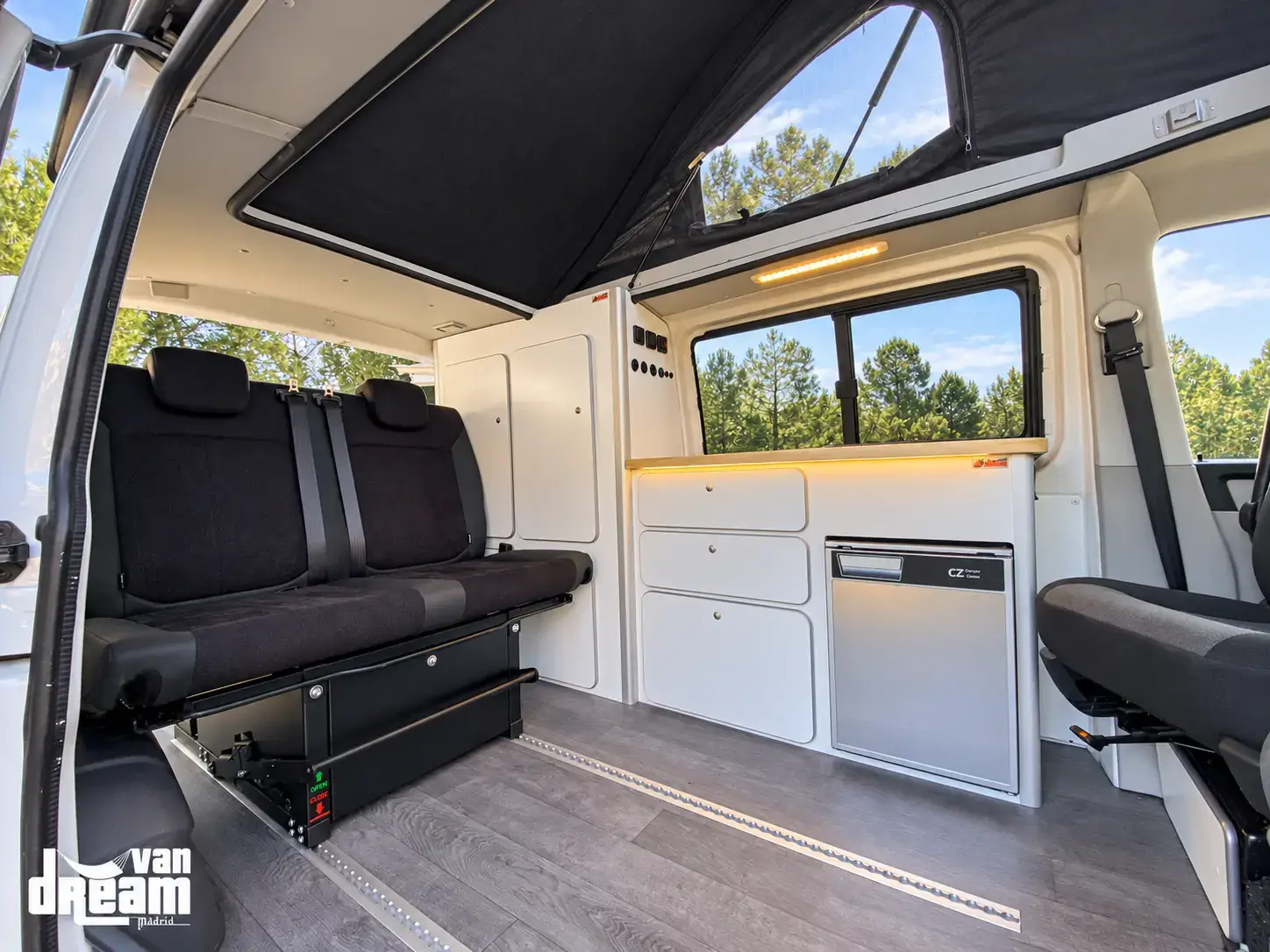 Interior de una furgoneta Van Dream Origin con asiento cama trasero, sistema de raíles, mobiliario a medida, nevera y techo elevable