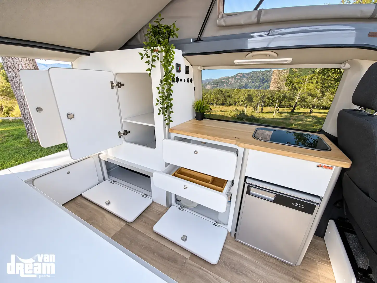 Interior de una furgoneta Van Dream Origin con mobiliario camper a medida, compartimentos abiertos, encimera de madera, fregadero y nevera