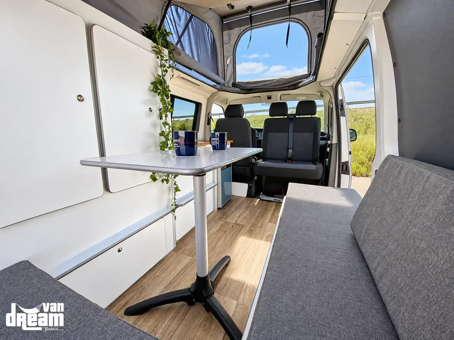 Interior de una furgoneta Van Dream Origin camperizada a medida, con mobiliario, mesa, asientos y techo elevable